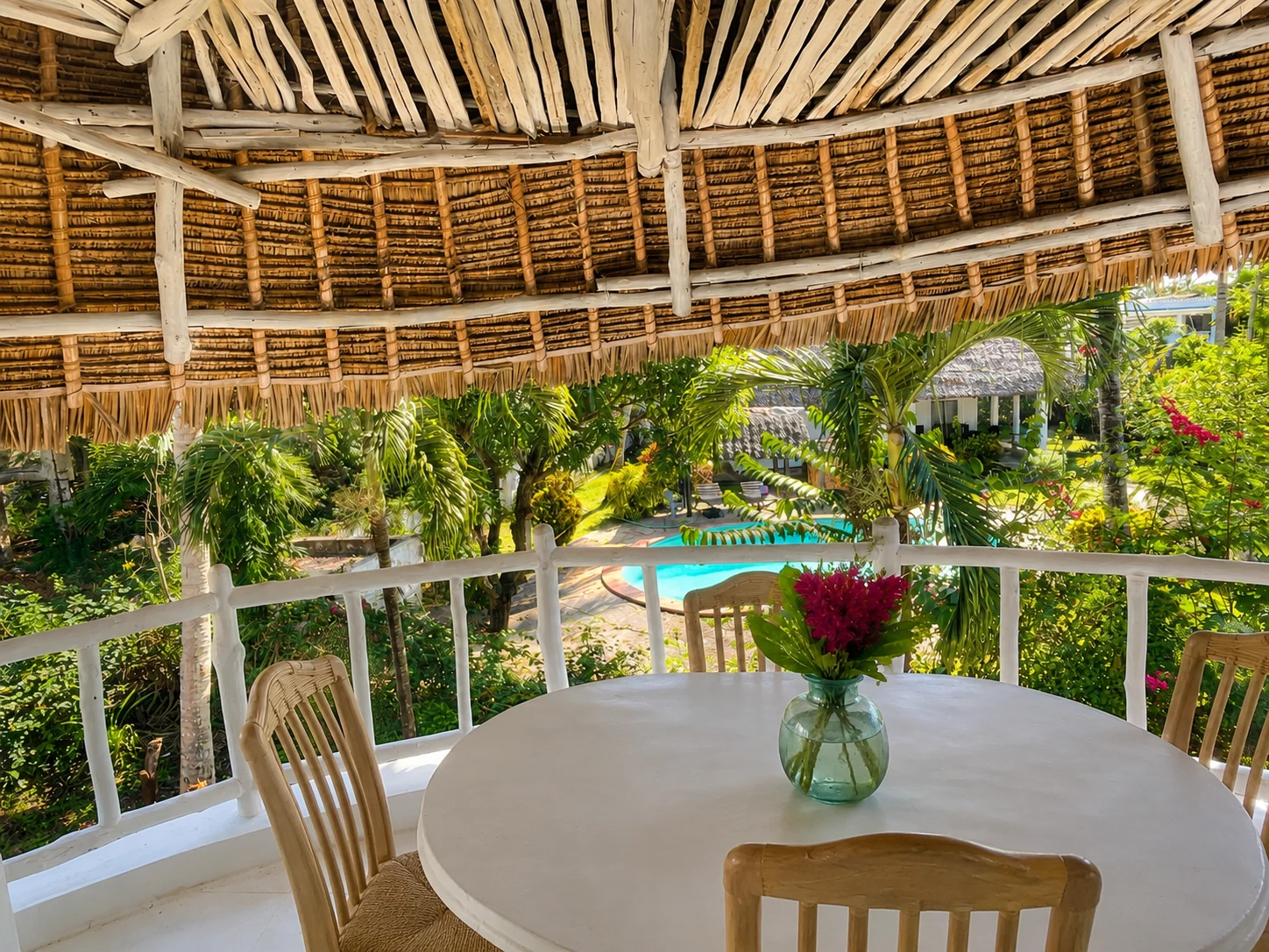 Thatched balcony at Cali Blossom Villa with a round dining table and flowers, looking over the tropical garden and pool