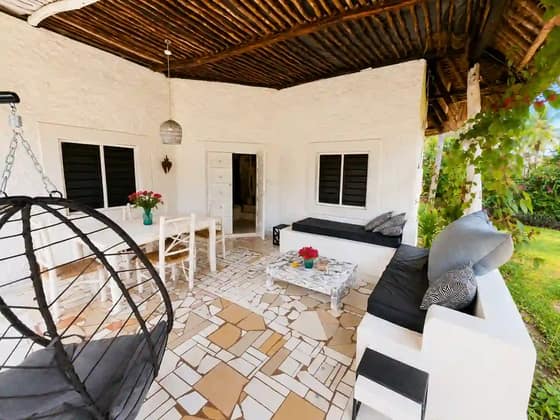 Covered terrace at Cali Blossom Villa with a white dining table, hanging chair and mosaic tile floor under a makuti roof
