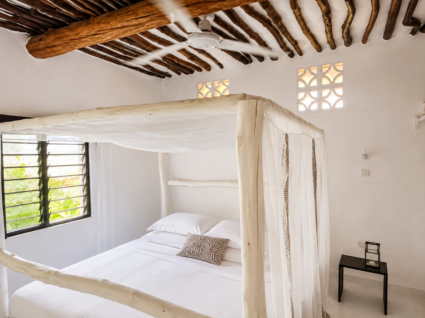 Bedroom at Cali Blossom Villa with a four-poster bed, mosquito net, ceiling fan and mangrove-pole ceiling