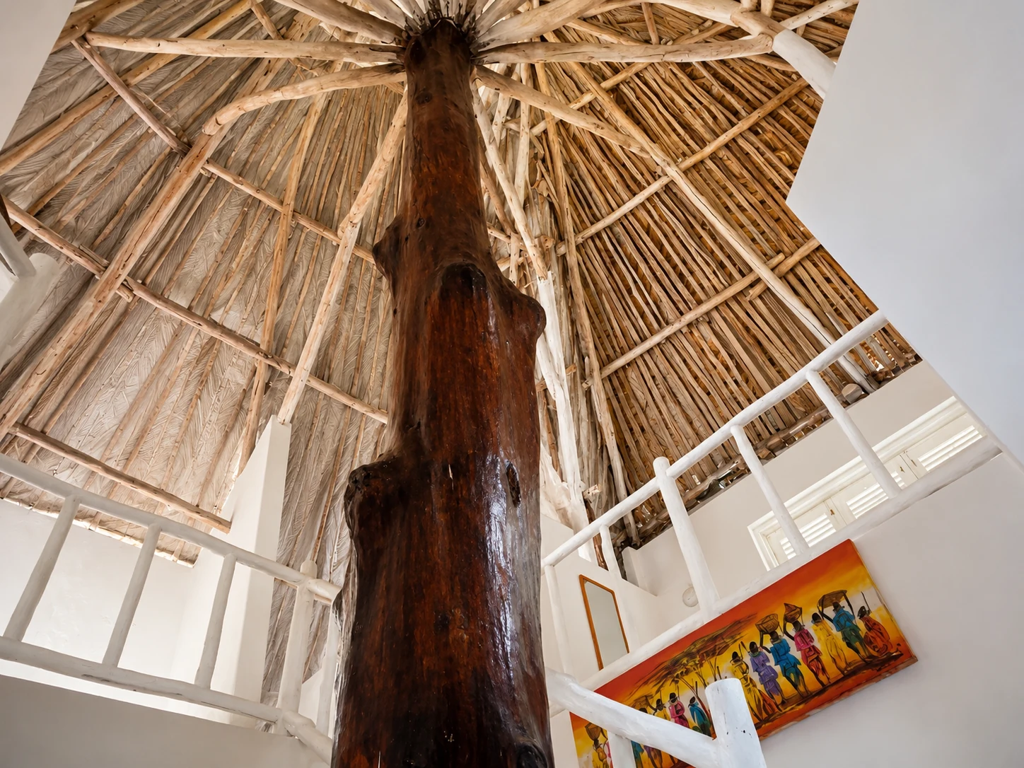 Soaring Swahili makuti roof at Cali Blossom Villa supported by a polished tree trunk above a white mezzanine